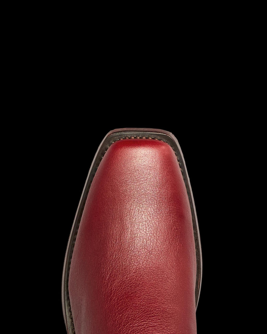 Close-up view of the toe of The Charlie Cowhide shoe in Scarlet red leather, featuring a square shape, dark sole edge, and visible cowhide texture, photographed against a white background.