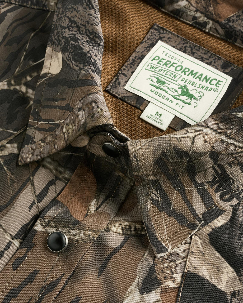 Close-up of a camouflage button-up shirt with a “Tecovas Performance Western Pearl Snap” label showing modern fit and size medium tags.
