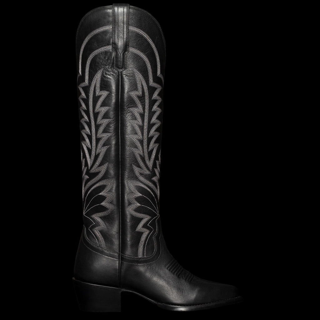 A tall black cowboy boot with intricate white stitching and a low heel, viewed from the side.