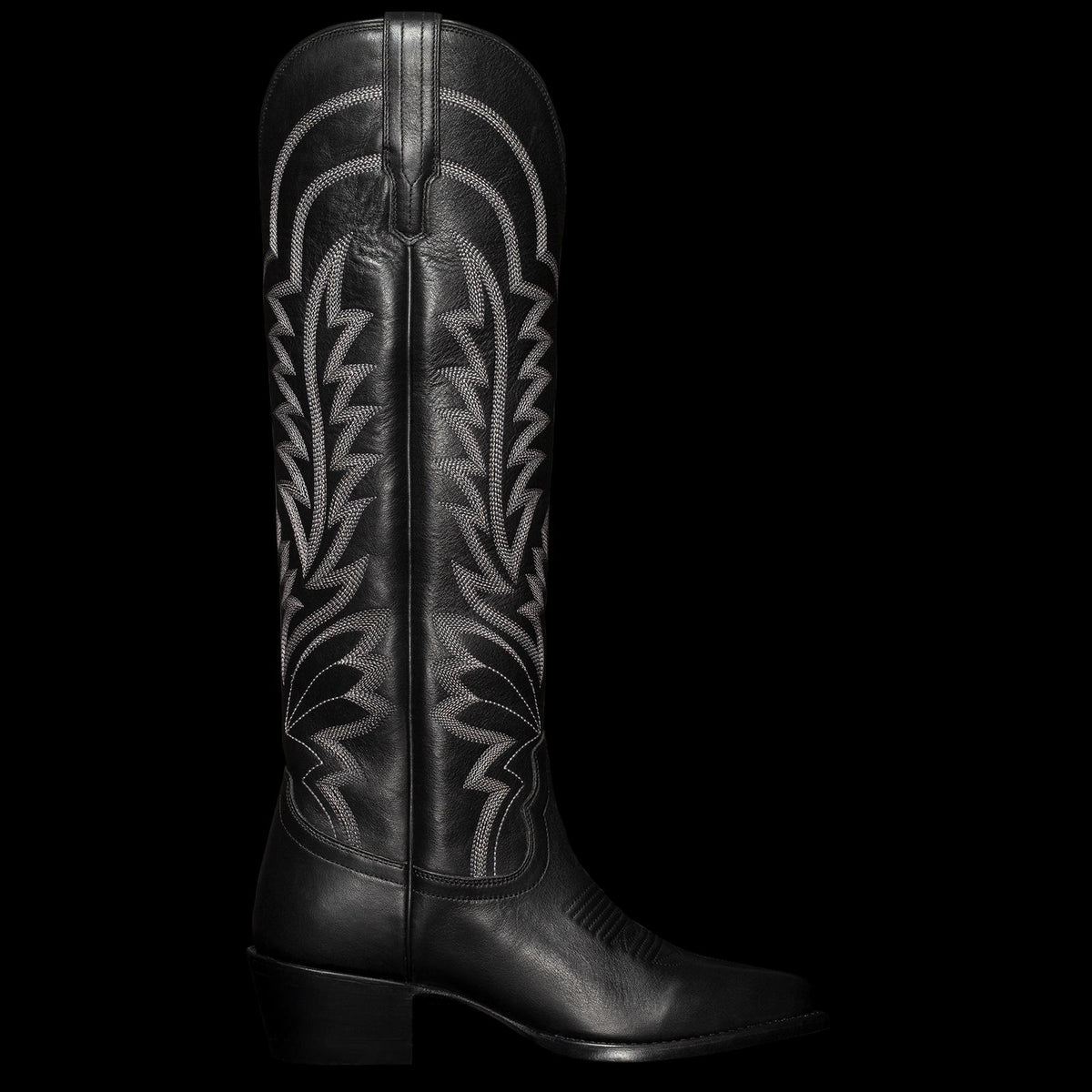 A tall black cowboy boot with intricate white stitching and a low heel, viewed from the side.
