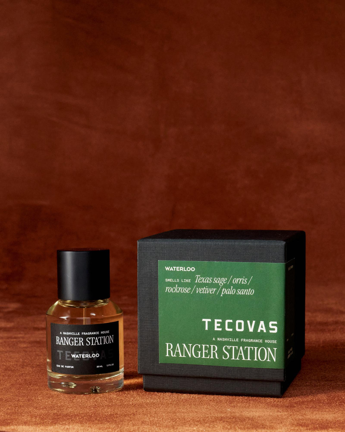 A bottle of Tecovas Ranger Station Waterloo fragrance sits next to its matching green and black box on a brown surface.