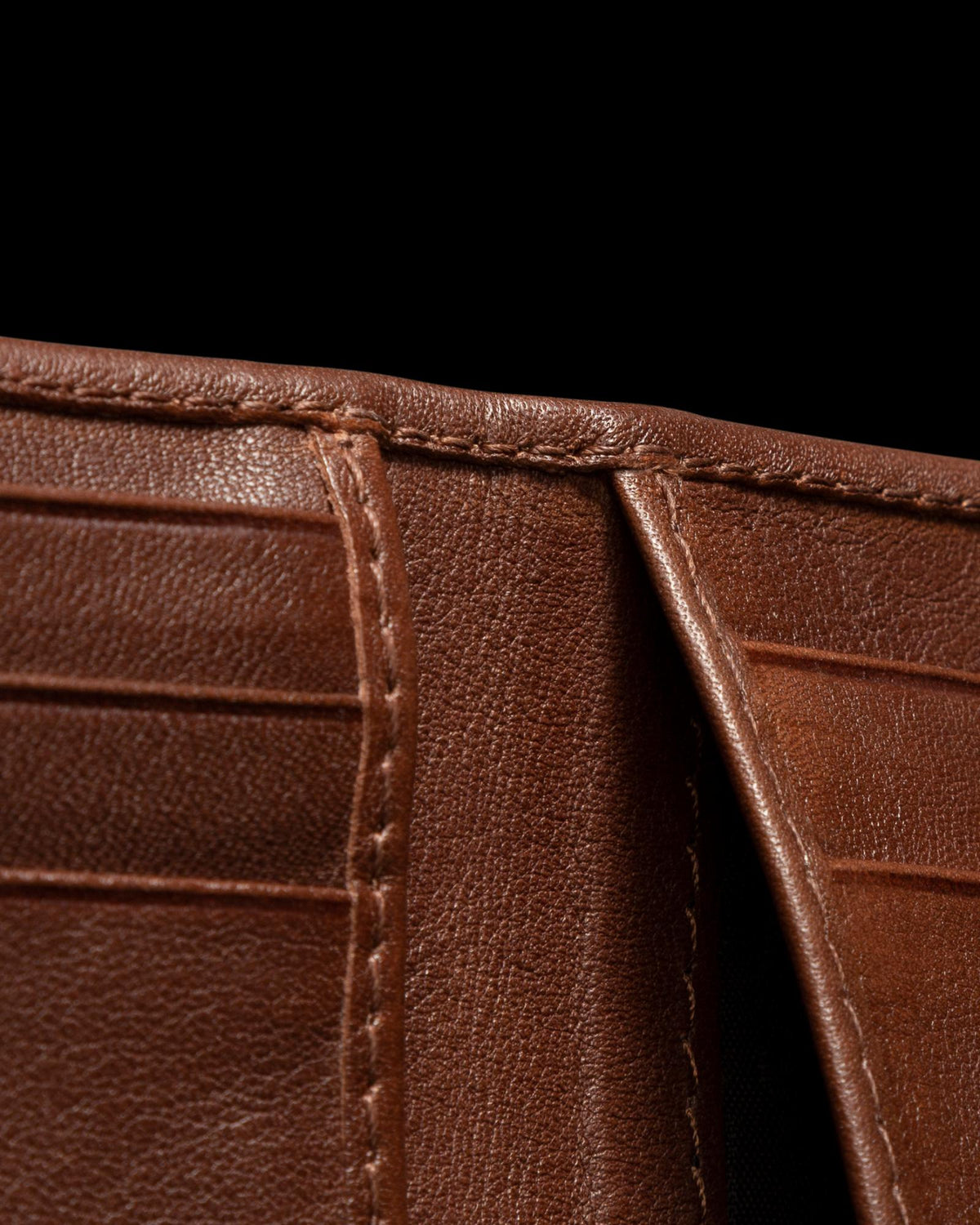 Close-up of an open brown leather wallet showing card slots and stitching details against a black background.