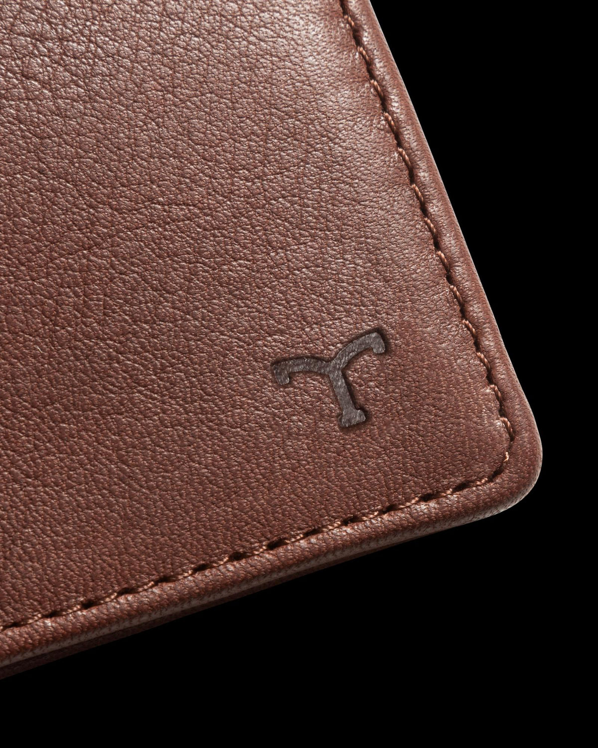 Close-up of a brown leather material with visible stitching and a small embossed logo in the corner.
