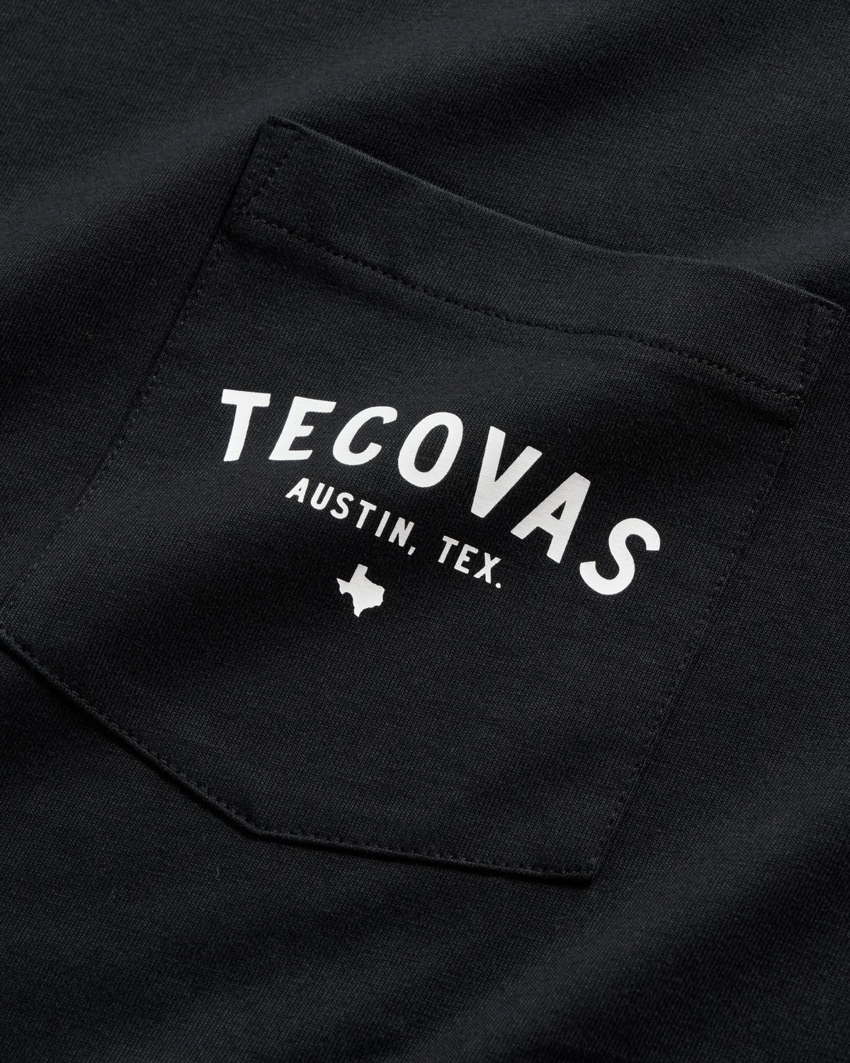 Close-up of a black shirt pocket with white text reading "Tecovas Austin, Tex." and a small Texas state outline below.
