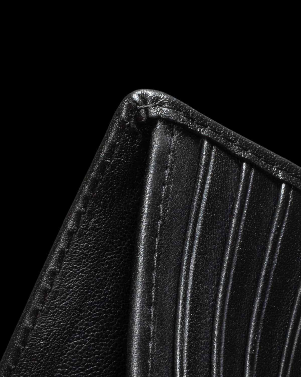 Close-up of a black leather wallet corner, showing stitching and vertical grooves, against a black background.