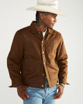 A man wearing a white cowboy hat and a brown canvas chore jacket over a white t-shirt and blue jeans.