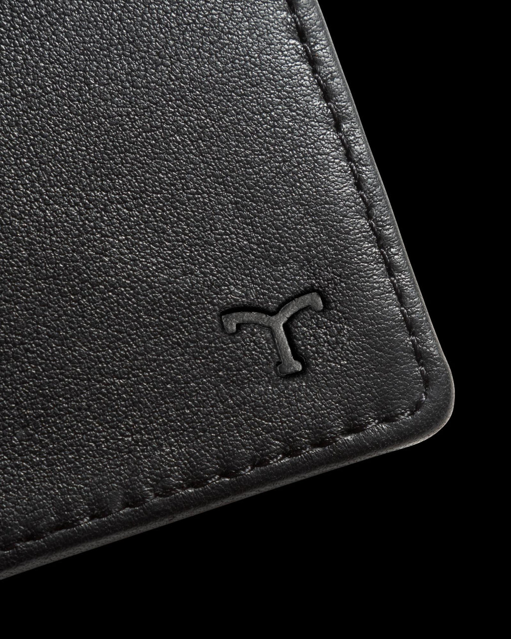 Close-up of a black leather wallet corner with an embossed "T" logo.
