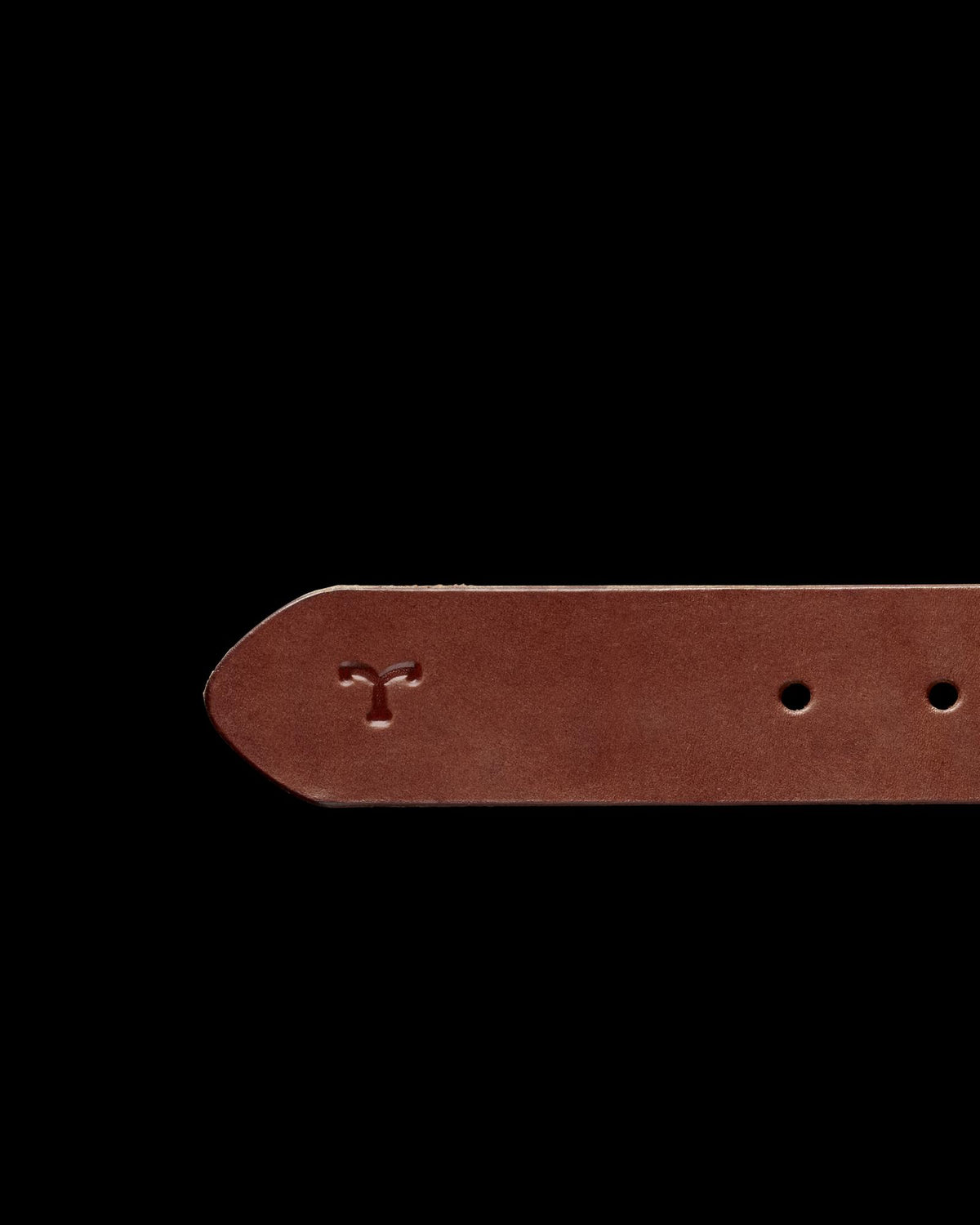 Close-up of a brown leather belt with a logo embossed near the end and two visible holes. The background is solid black.
