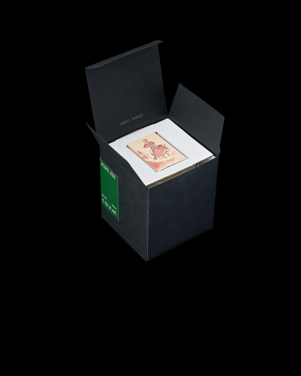 An open black box containing a book with an illustrated cover featuring a person. The box has a green label and white interior padding.