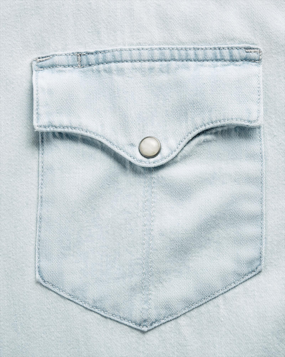 Close-up of a light blue denim shirt pocket with a flap and a metal snap button.
