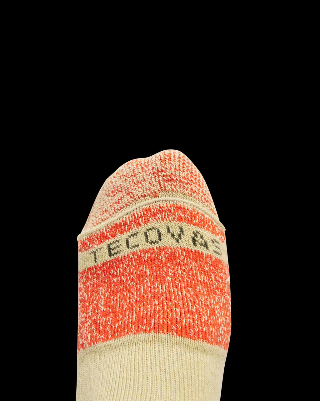 A close-up of a beige and orange sock with the partially visible text "TECOV" on the toe, set against a black background.