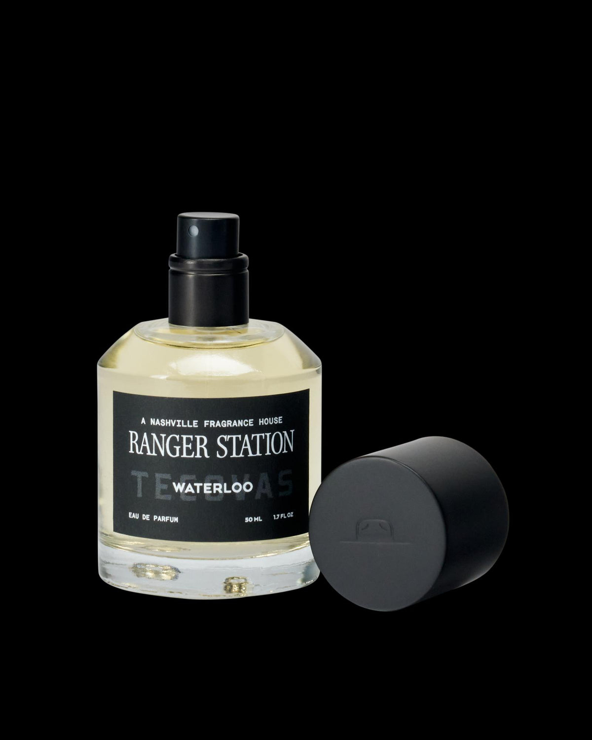 A bottle of Ranger Station Waterloo Eau de Parfum with a black spray nozzle and detached black cap placed beside it.