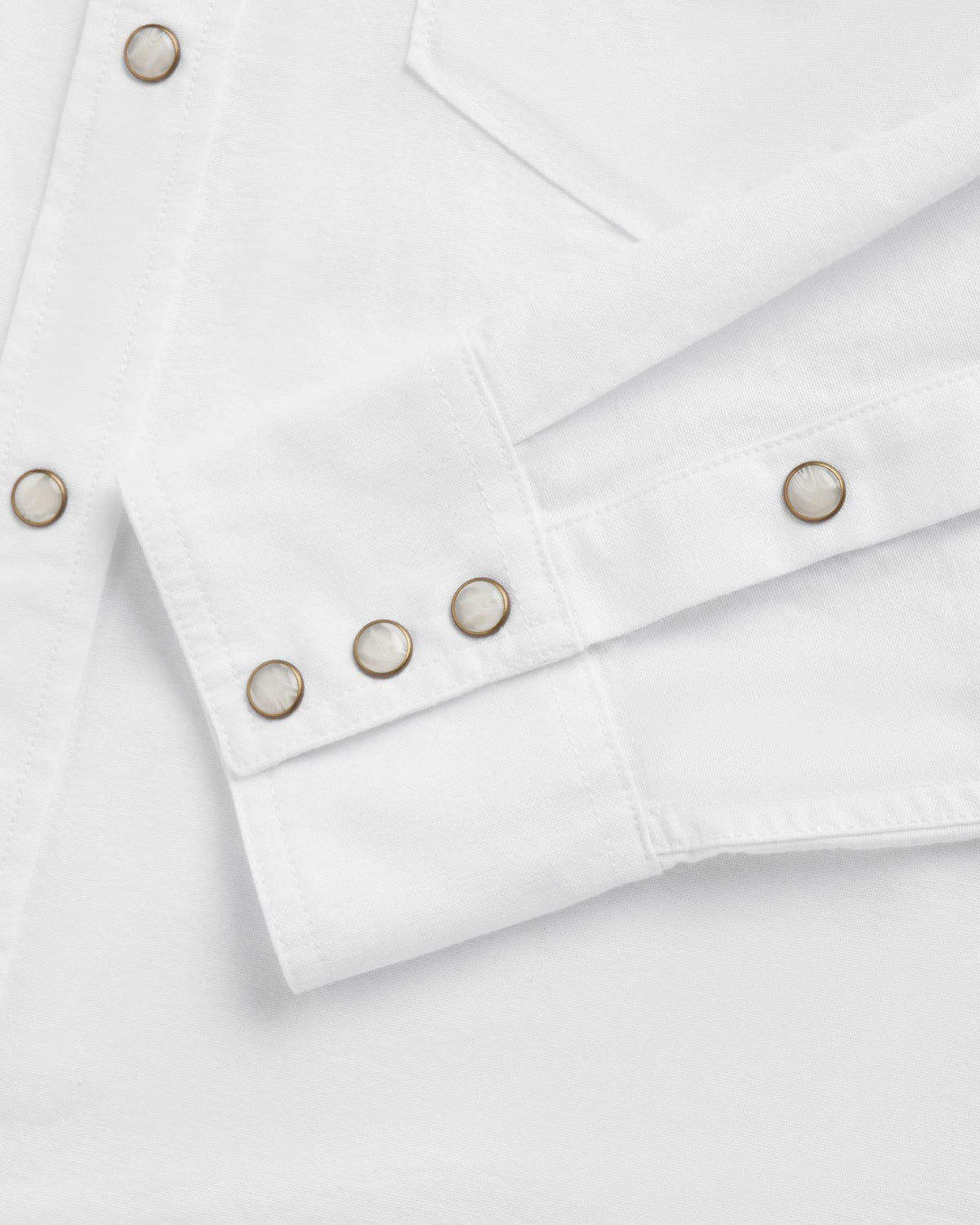 Close-up of a white long-sleeve shirt featuring metal snap buttons on the cuff and front placket, along with a visible chest pocket seam.