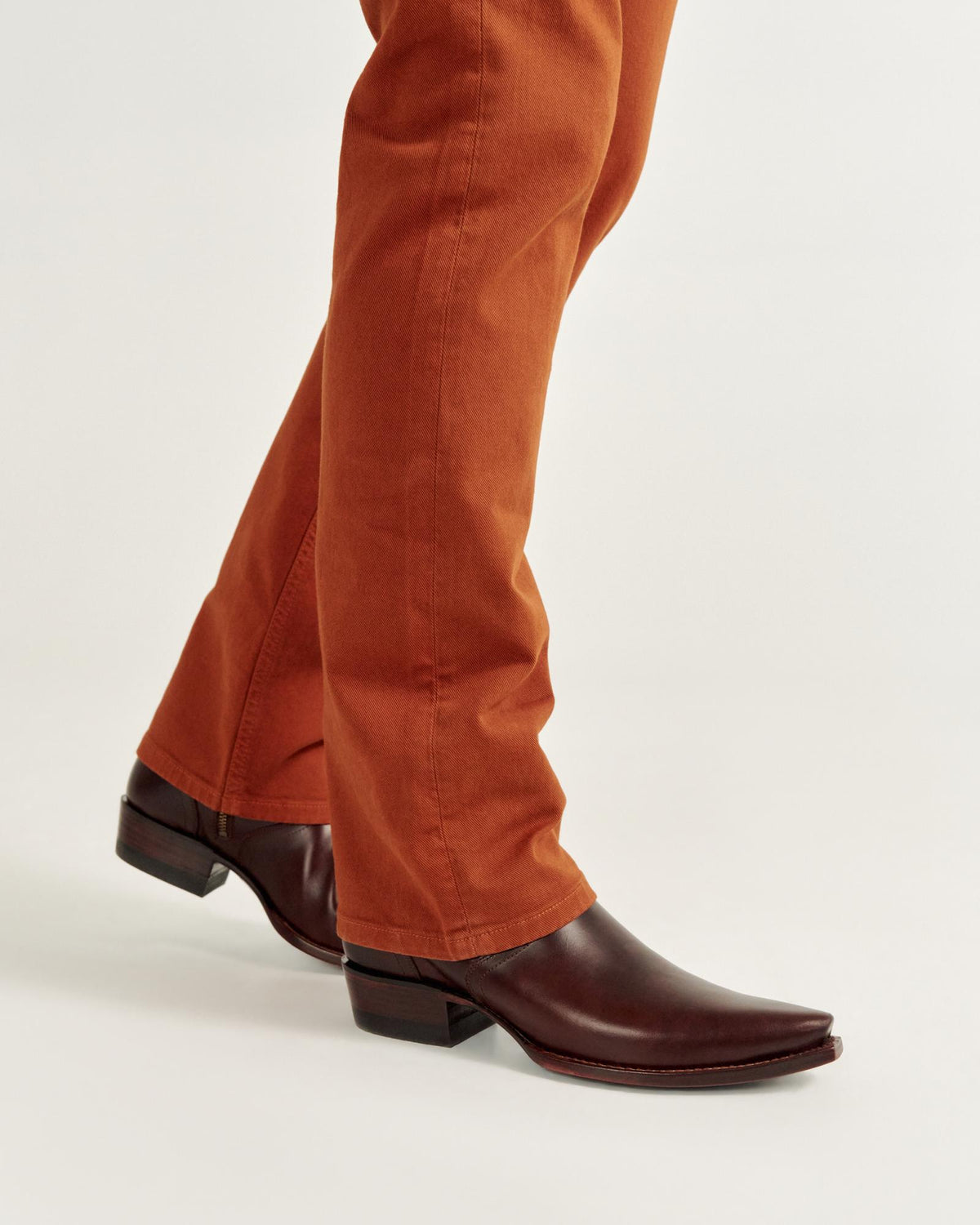 Person wearing orange pants and brown leather boots against a plain background.