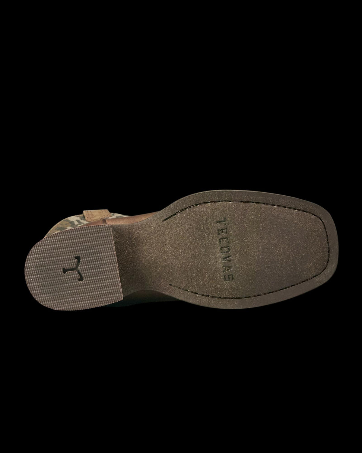 Bottom view of a brown shoe with a textured heel and a grooved marking, “TEJONAS,” stamped on the sole.