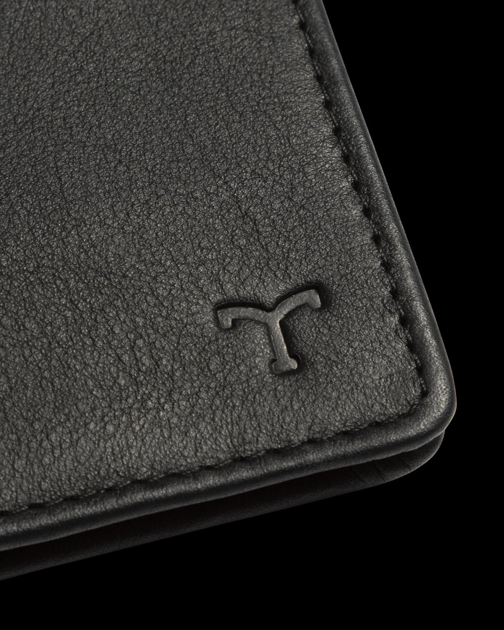 Close-up of a black leather wallet corner with a T logo embossed on the surface.
