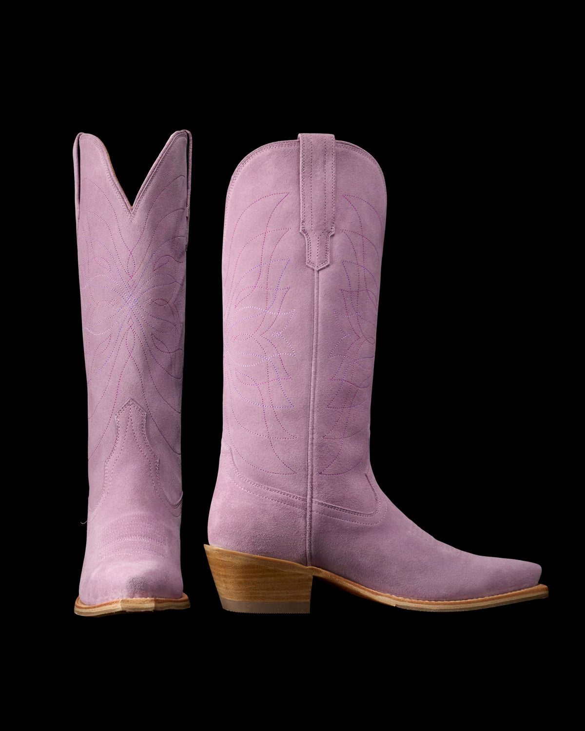 The Annie in Lavender Suede. Pair of tall, light purple Annie Suede cowboy boots with pointed toes, wooden heels, and decorative stitching, shown from side and front angles on a white background.