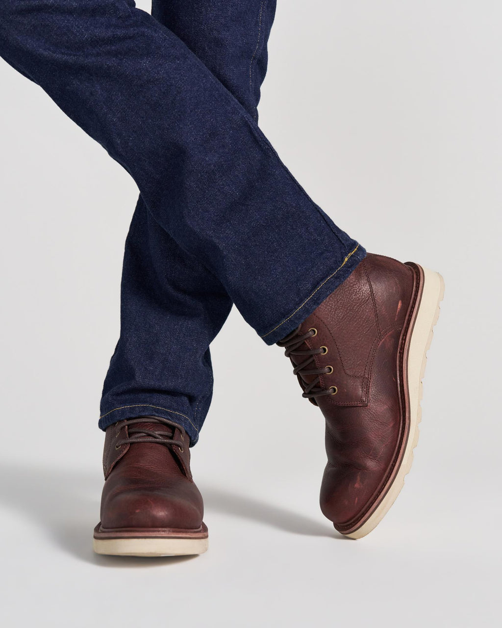 The Knox Lace Up in Cognac Cowhide. A person wearing dark blue jeans and cognac cowhide leather lace-up boots with light-colored soles.