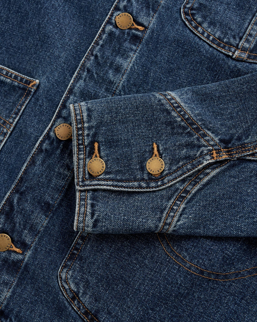 Close-up of a blue denim jacket showing a sleeve with three metal buttons and visible stitching.