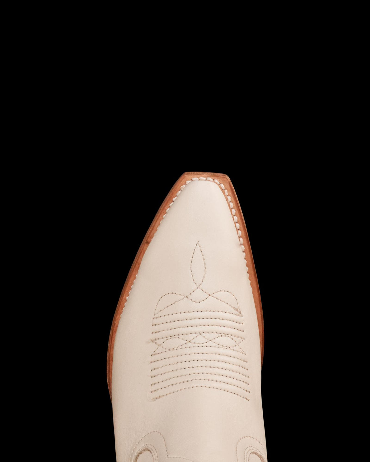 Close-up of a white cowboy boot with intricate stitching on the toe, featuring a brown sole.