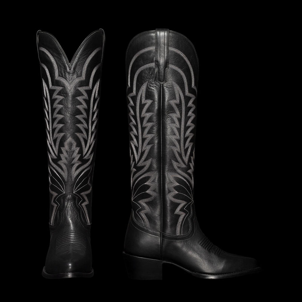 Black cowboy boots with intricate white stitching, featuring a pointed toe and a chunky heel, displayed upright and in profile.