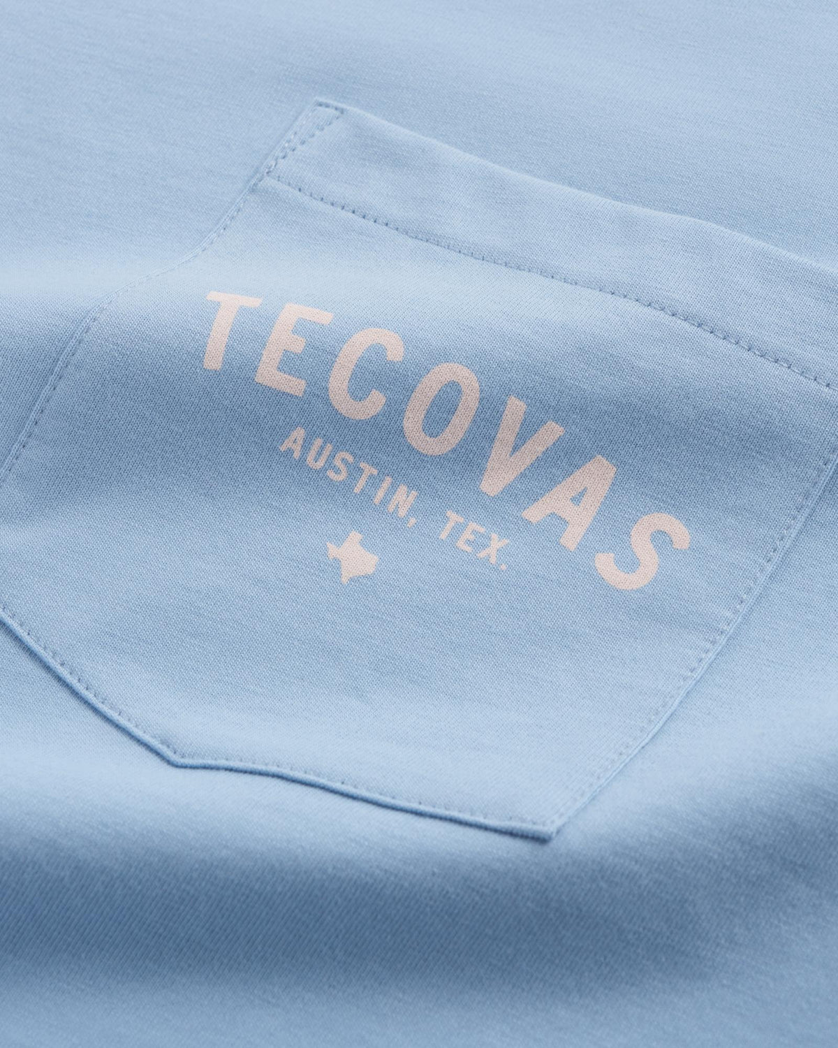 Close-up of a light blue shirt pocket with the words "TECOVAS AUSTIN, TEX." and a small Texas outline printed in white.