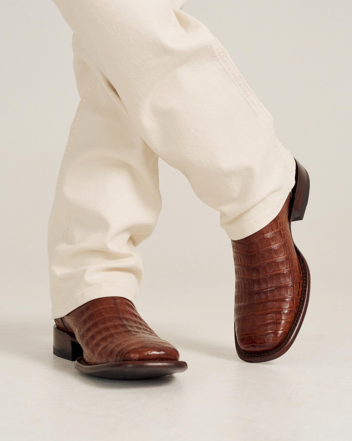 Close up of a person wearing cream pants and The William Caiman cowboy boots in rich Dark Pecan Caiman leather.