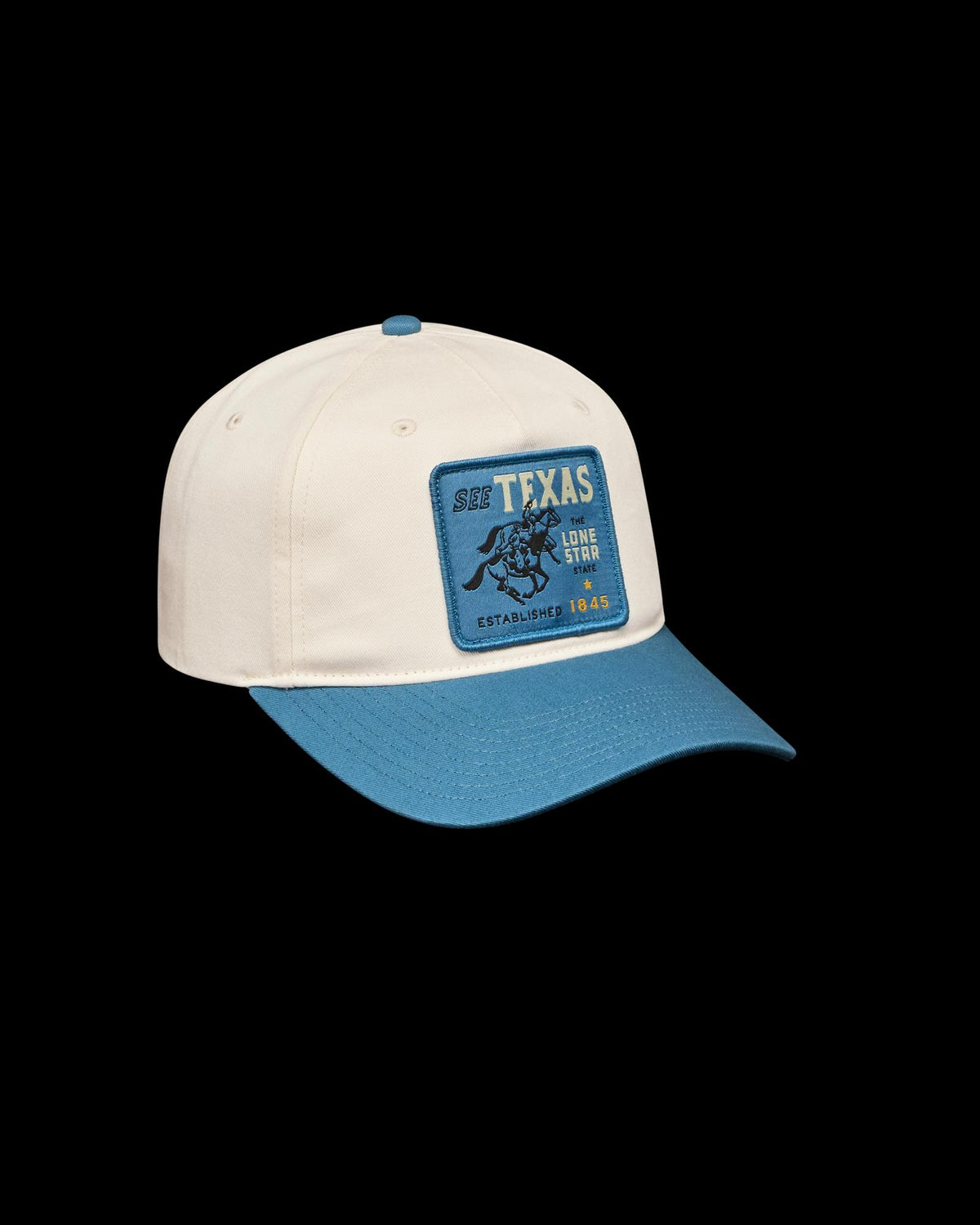 A cream-colored baseball cap with a blue brim and a blue patch reading "SEE TEXAS LONE STAR ESTABLISHED 1845" featuring an illustration of a bucking horse.