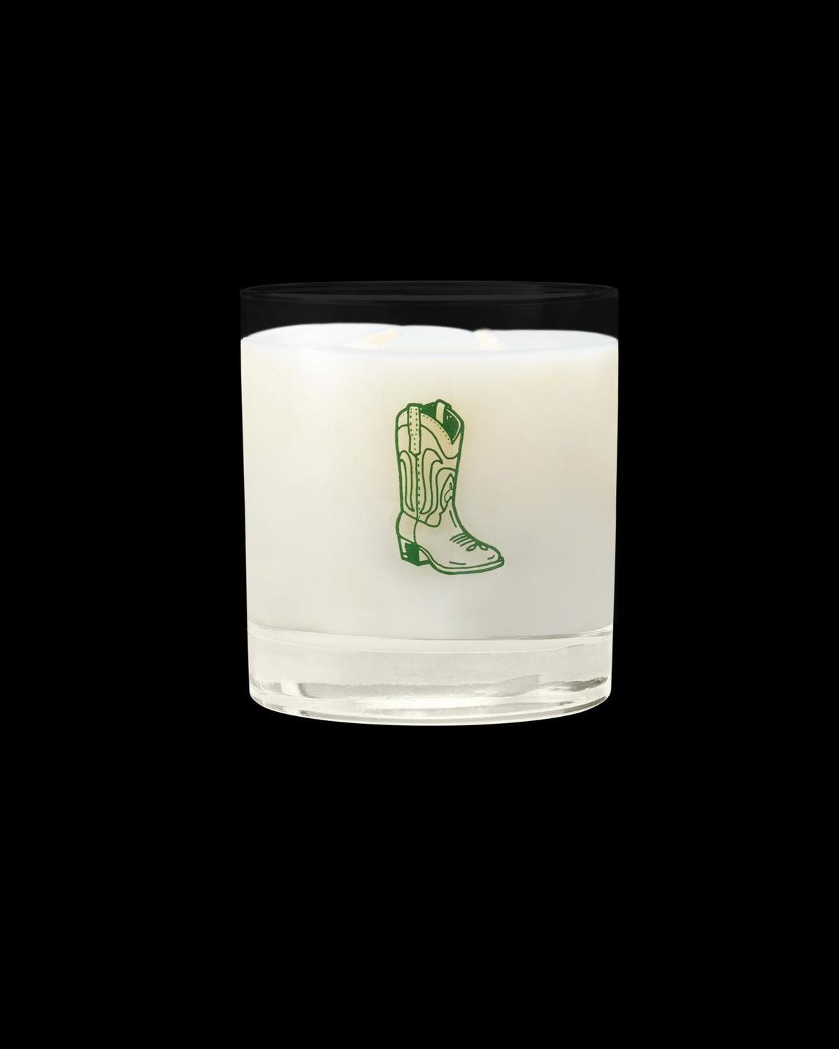 A white candle in a clear glass holder with a green illustration of a cowboy boot on the front.